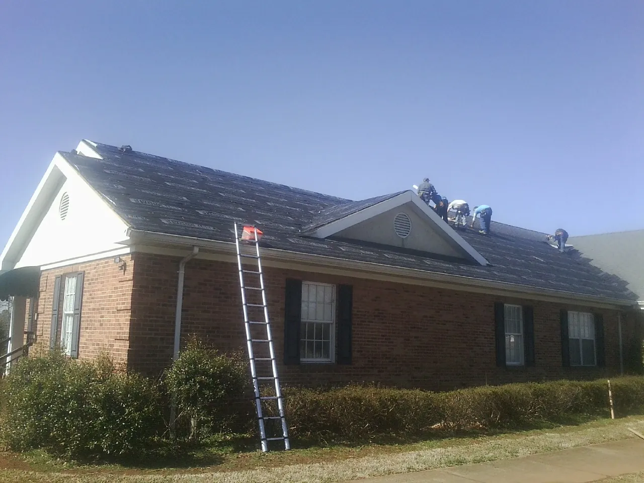 Crew tearing shingles off a brick ranch roof with a ladder set — Emergency Roof Repair work by our crew in Rahway