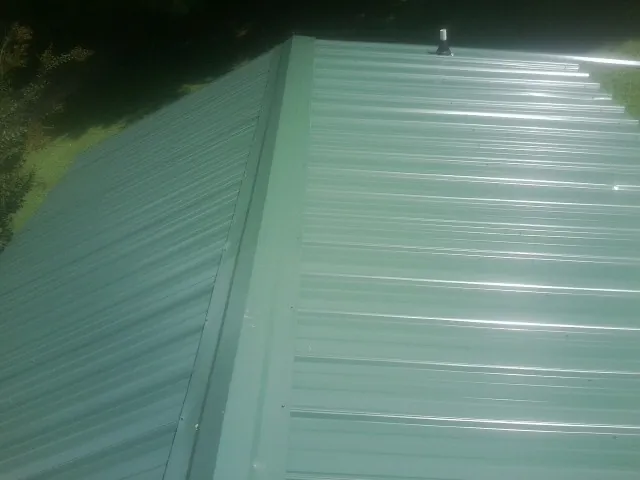 New green metal panels meeting at the ridge of a roof — Flat Roof Repair work by our crew in Rahway