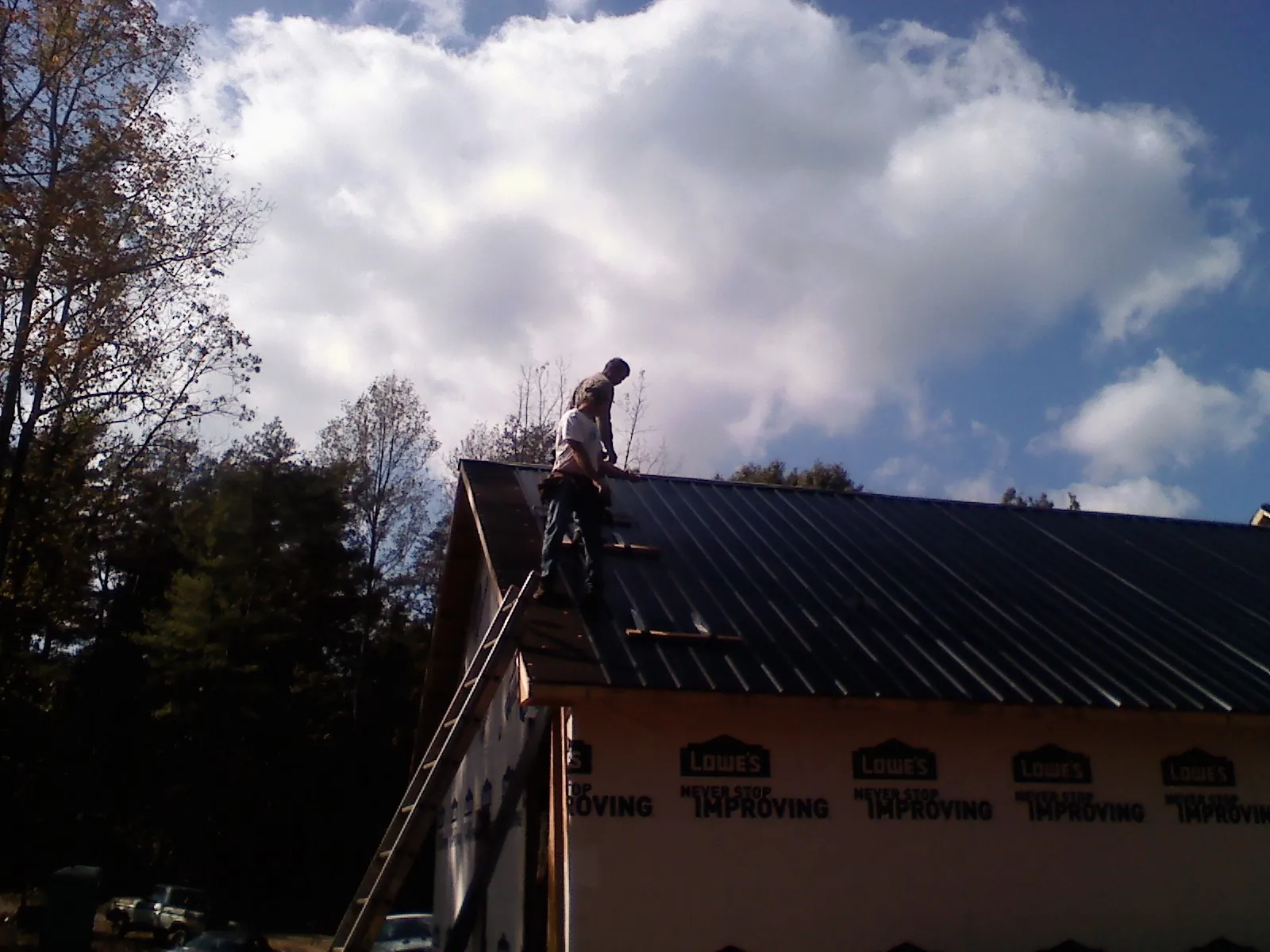 Roofer fastening dark metal panels high against a cloudy sky, from a Roof Inspection job in Rahway