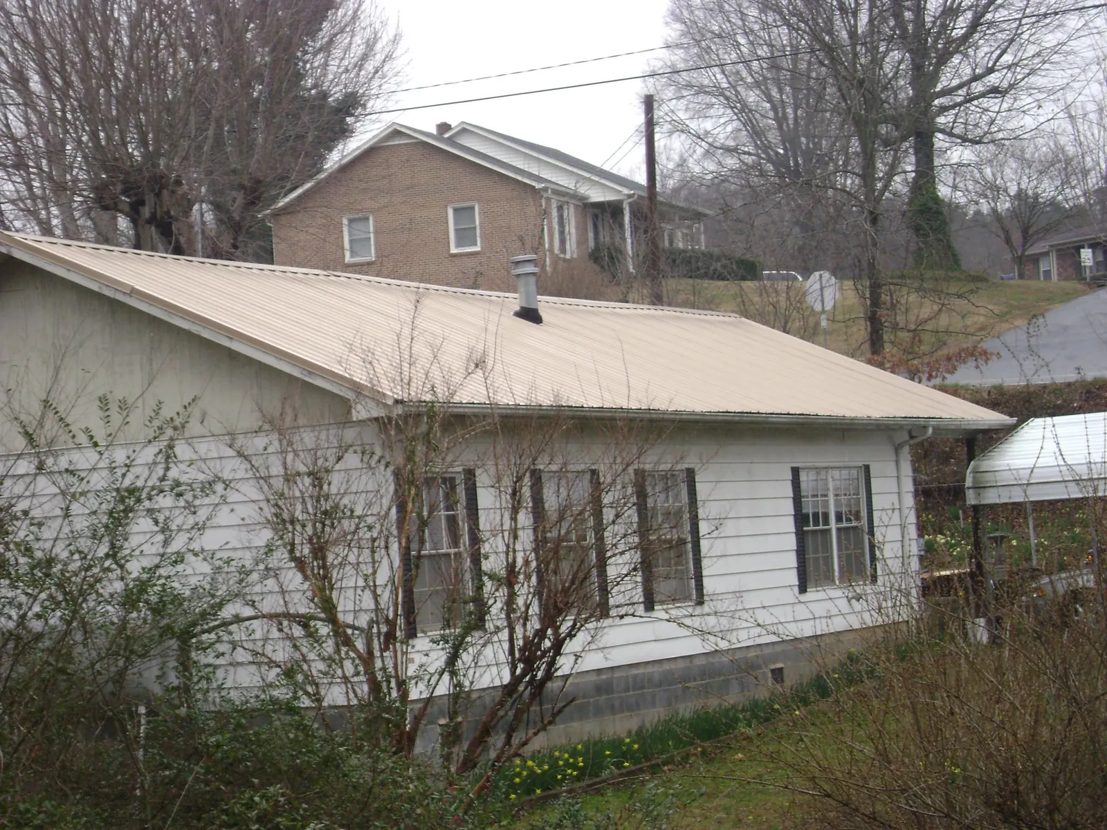 Tan metal roof on a white sided house set into a hillside — Commercial Roofing by Roofing Brothers in Rahway